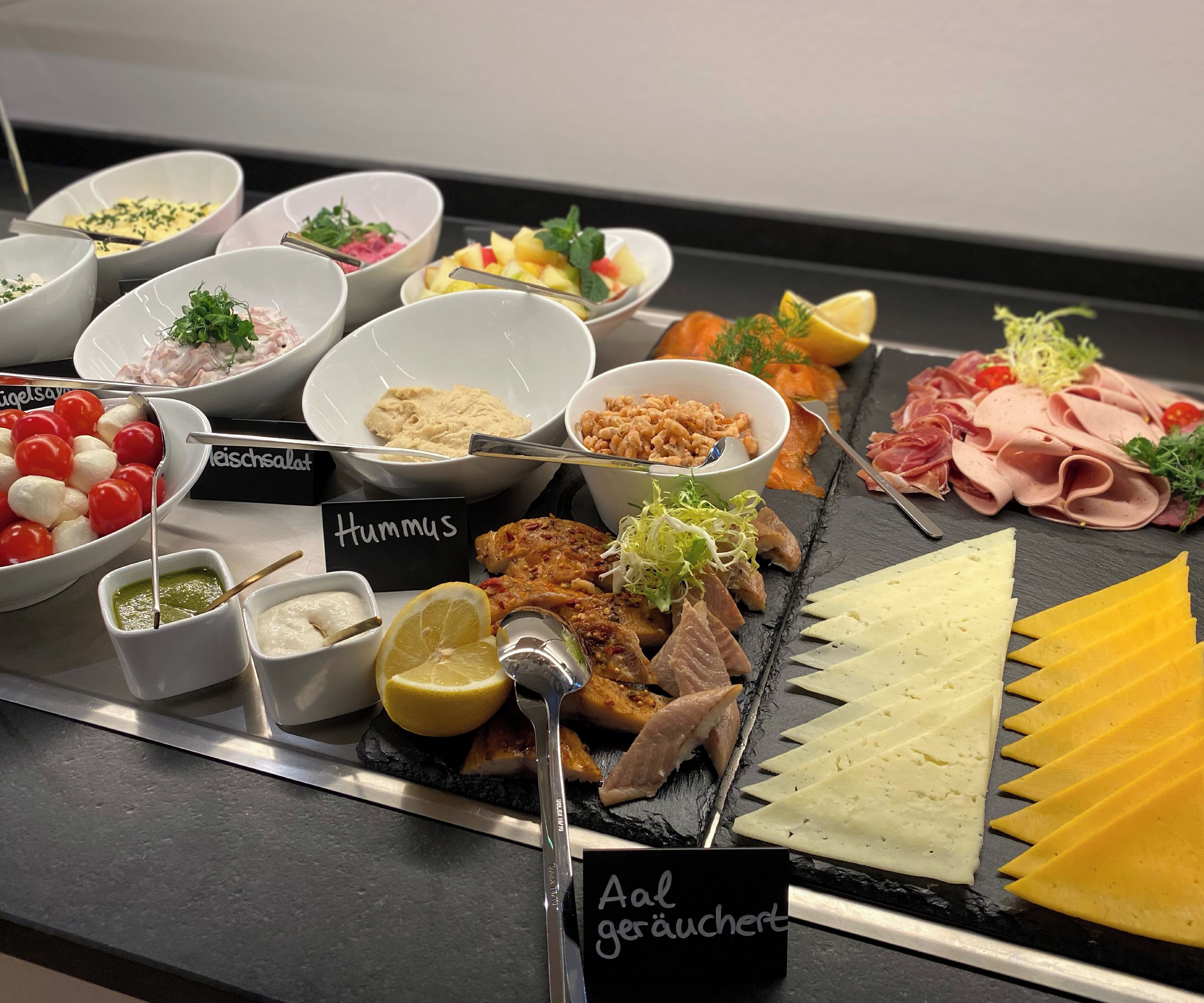 Un bufé con diversos platos, incluyendo hummus, carne, queso y verduras.