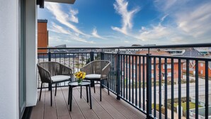 A balcony with two wicker chairs, a small table, and a vase of flowers.