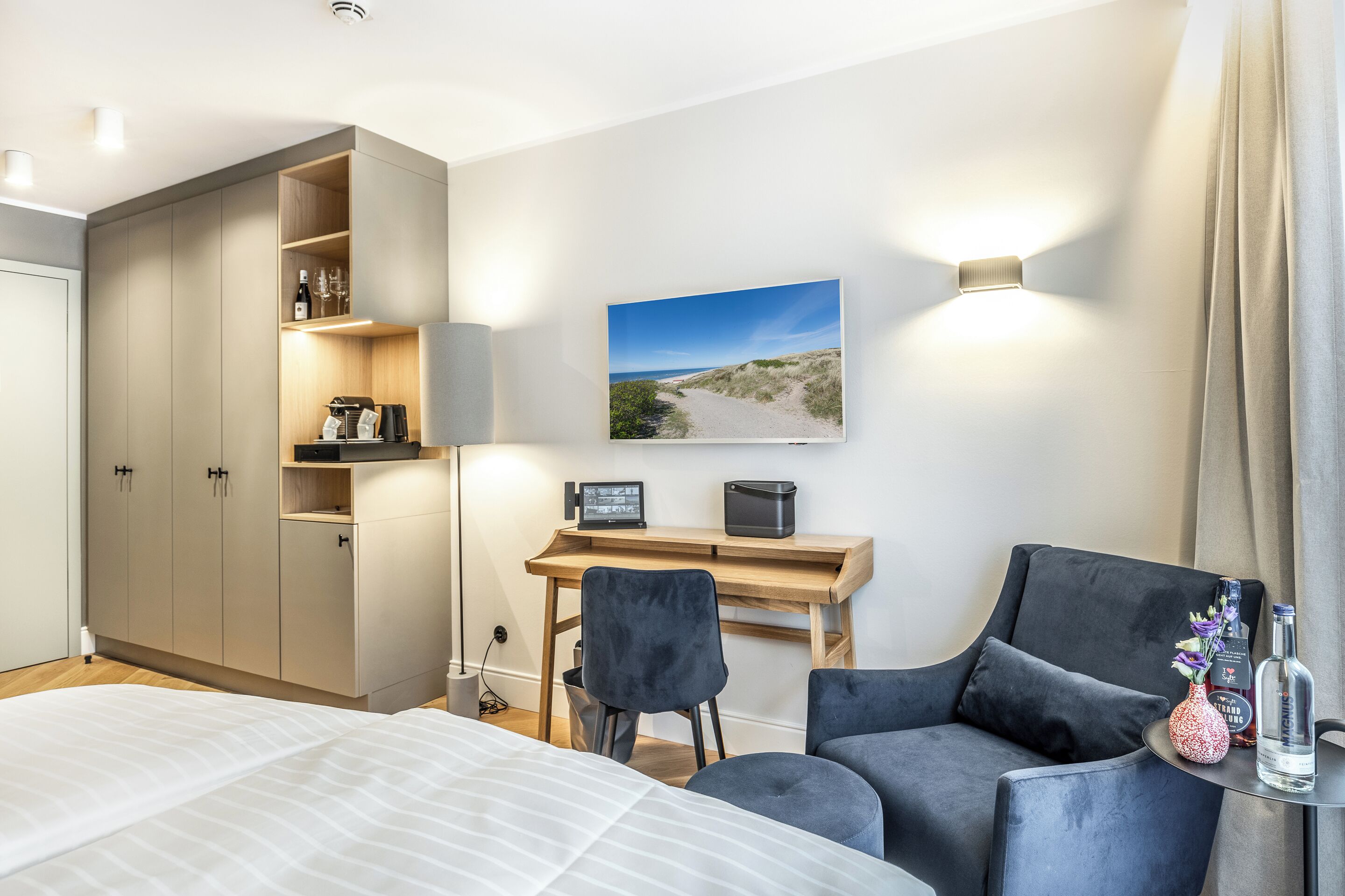 Una habitación de hotel moderna con una cama, un escritorio con una silla, un armario y un cuadro de una playa.