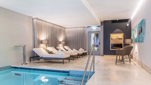 A modern indoor swimming pool area with lounge chairs, a seating area, and a staircase leading to a higher level.