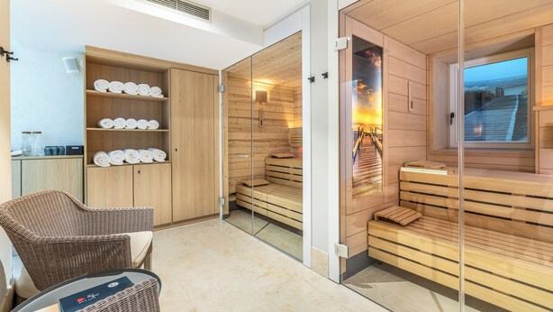 A modern spa room with wooden benches, a glass partition, and a wicker chair.