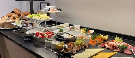 A buffet with various food items including meats, cheeses, fruits, and condiments.