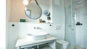 A modern bathroom with a large oval sink, a round mirror, and a glass-enclosed shower.