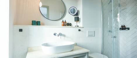 A modern bathroom with a large oval sink, a round mirror, and a glass-enclosed shower.