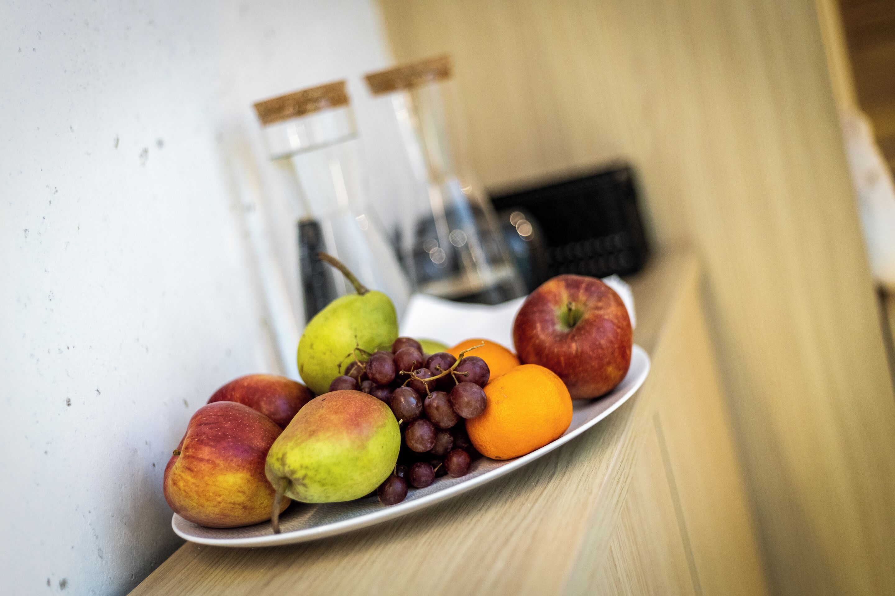 A plate of fruits including apples, pears, grapes, and oranges on a wooden table.