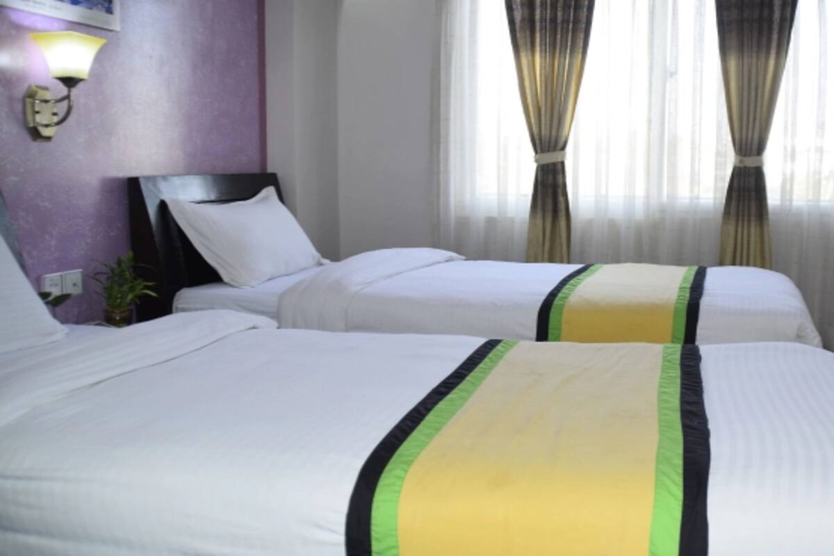 A hotel room with two beds, a nightstand, a lamp, and a window with curtains.