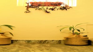 A bathroom with two brass vases on marble flooring, a yellow wall, and a window with blinds. - MeroStay 260 Hotel Rate (Kathmandu)
