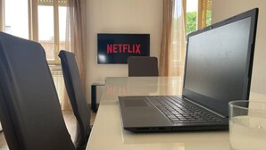 A room with a laptop on a table, a TV displaying 'NETFLIX', and a glass of water.