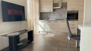 A modern kitchen with a built-in oven, a dining area with a black chair, and a flat-screen TV mounted on the wall.