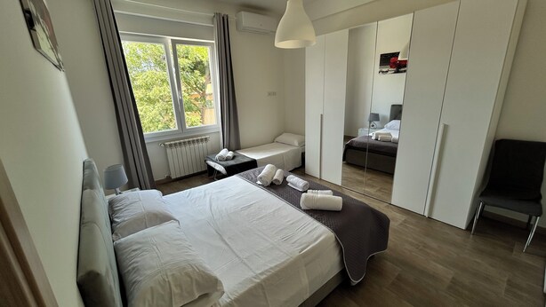 A hotel room with a large bed, a desk, a chair, and a wardrobe.
