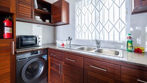 A modern kitchen with wooden cabinets, a built-in washing machine, a microwave, and a double sink. - Crystal Shores Self Catering Apartments - Seychelles (Mahé Island)