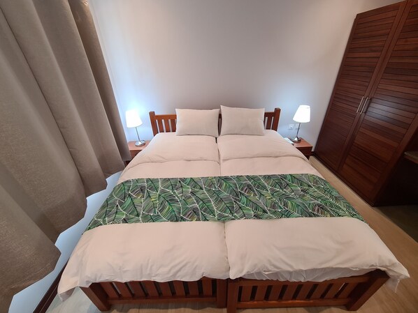 Uma cama bem arrumada com um cobreleto estampado, duas luminárias de cabeceira e um guarda-roupa de madeira.