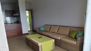 A living area with a sofa, a coffee table, and a kitchen in the background. - Crystal Shores Self Catering Apartments - Seychelles (Mahé Island)