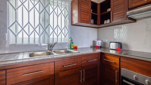 A kitchen with wooden cabinets, a stainless steel sink, a Bosch coffee maker, and a Bosch dishwasher. - Crystal Shores Self Catering Apartments - Seychelles (Mahé Island)