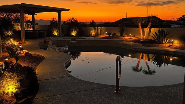 Un área de piscina con una pérgola, palmeras y vistas al atardecer.