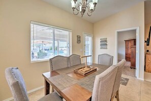 Uma sala de jantar com uma mesa de madeira, seis cadeiras, um candelabro e uma janela com persianas.
