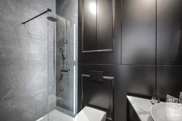 A modern bathroom with a glass-enclosed shower, dark cabinetry, and a marble countertop. - City Lights Skawińska (Kraków)