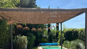 Ein überdachter Außenbereich mit Pool im Hintergrund.