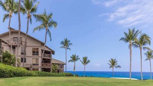 A beachfront hotel with a two-story structure, a balcony on the upper floor, and a well-maintained lawn in the foreground.