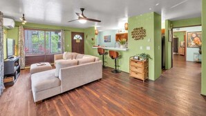 A spacious living room with a sofa, a ceiling fan, and a kitchen area visible in the background.