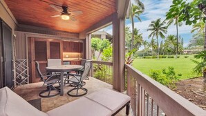 A covered outdoor seating area with a table and chairs, a ceiling fan, and a view of a green landscape with palm trees.