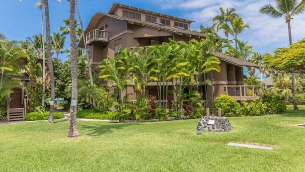A multi-story hotel with a flat roof, surrounded by lush greenery and palm trees.