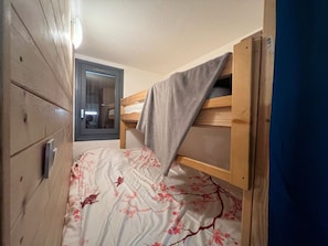 A small, narrow room with a bunk bed, a wooden wardrobe, and a door leading to a bathroom.