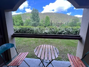 A balcony with two wooden tables and chairs, a view of a green landscape with trees and a hill in the background.