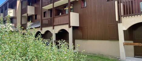 Un edificio de varios pisos con balcones, techo plano y un área ajardinada.
