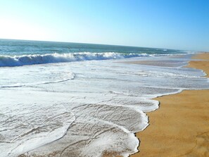 Une plage où les vagues viennent lécher le rivage, un ciel dégagé et une étendue de sable.