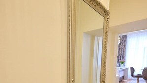 Ein großer, aufwendig gestalteter Spiegel mit goldener Rahmung an einer Wand in einem Raum mit hellem Boden und einem Stuhl im Hintergrund.