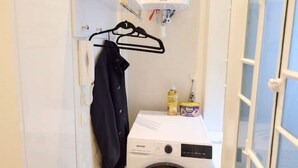Ein kleiner Waschraum mit einer Frontlader-Waschmaschine, einem Wäscheständer und einem Warmwasserbereiter.