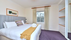 Habitación de hotel con cama, mesita de noche, lámpara, ventana con cortinas y vistas a árboles.