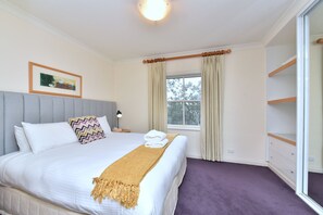 Habitación de hotel con cama, mesita de noche, lámpara, ventana con cortinas y vistas a árboles.