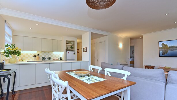 Una cocina moderna con armarios blancos, una mesa de comedor con sillas y una sala de estar con sofá.