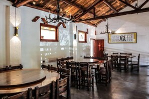 A restaurant interior with wooden tables and chairs, a high ceiling with exposed beams, and wall-mounted artwork.
