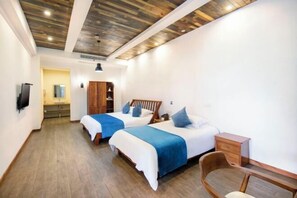 A hotel room with two beds, wooden flooring, a wooden ceiling, a small desk, and a chair.