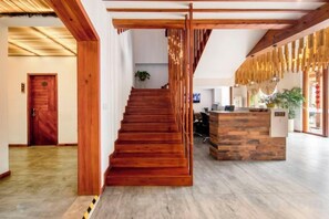 A wooden staircase leading to a reception desk in a modern interior with a wooden floor and a plant in the background.