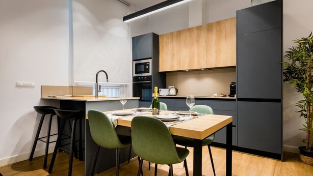 A modern kitchen with a wooden dining table, green chairs, and a built-in oven. - In the heart of Seville by RentalSevilla (Sevilla)