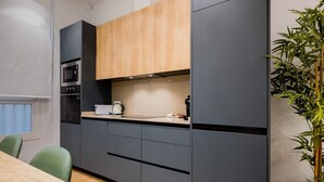 A modern kitchen with dark cabinetry, a wooden upper cabinet, and a built-in oven. - In the heart of Seville by RentalSevilla (Sevilla)