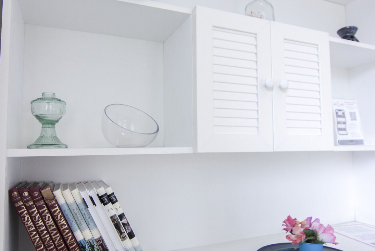 Un gabinete blanco con dos puertas, un cuenco de vidrio y un pequeño jarrón azul con flores.