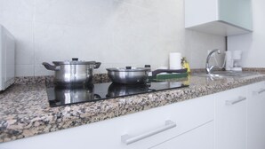 A kitchen with white cabinets, a granite countertop, two stainless steel pots on an induction cooktop, a coffee maker, and a glass cabinet above the sink. - RentalSevilla in the Triana neighbourhood (Sevilla)