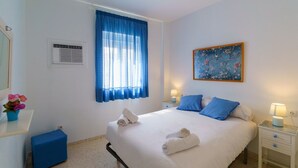 A neatly arranged bedroom with a bed, bedside tables, a window with curtains, a wall-mounted air conditioner, and a framed picture. - RentalSevilla in the Triana neighbourhood (Sevilla)