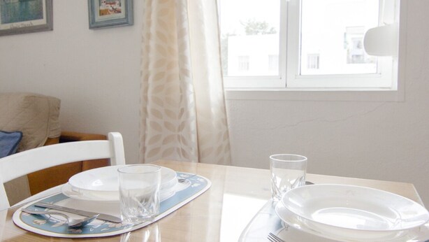 A dining table set with plates, glasses, and cutlery, a window with curtains, and a framed picture on the wall. - RentalSevilla in the Triana neighbourhood (Sevilla)