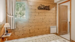 Ein Schlafzimmer mit Holzvertäfelung, einem Bett, einem Nachttisch, einer Lampe, einem Fenster mit Vorhängen, einer Tür und einem Wandheizkörper.