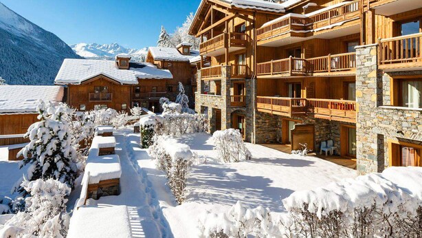 Eine Holzhütte mit mehreren Balkonen und einer Steinfassade, umgeben von schneebedeckten Bäumen und Bergen.