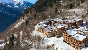 Eine Gruppe Holzhütten mit schneebedeckten Dächern, vor einer Kulisse aus schneebedeckten Bergen und dichtem Wald.