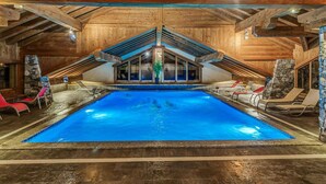 Ein Hallenbad mit Holzbalkendecke und Steinwänden, umgeben von Liegestühlen.