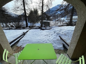 A green table and bench set in a snowy outdoor area with a mountain view.