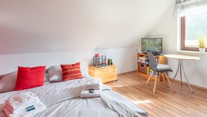 A bedroom with a bed, pillows, a wooden dresser, a desk with a chair, a television, and a window with a plant. - Gode Sünn vacation apartment in Tating for up to 4 people (Tating)